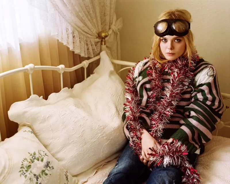 Elle Fanning, pózující v posteli, má na sobě rozmarný vzhled s pruhovaným svetrem