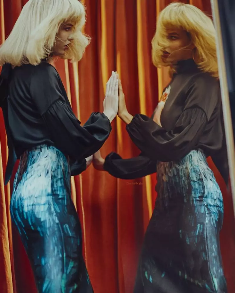 En se regardant dans le miroir, Karlie Kloss porte un chemisier noir et une jupe métallique