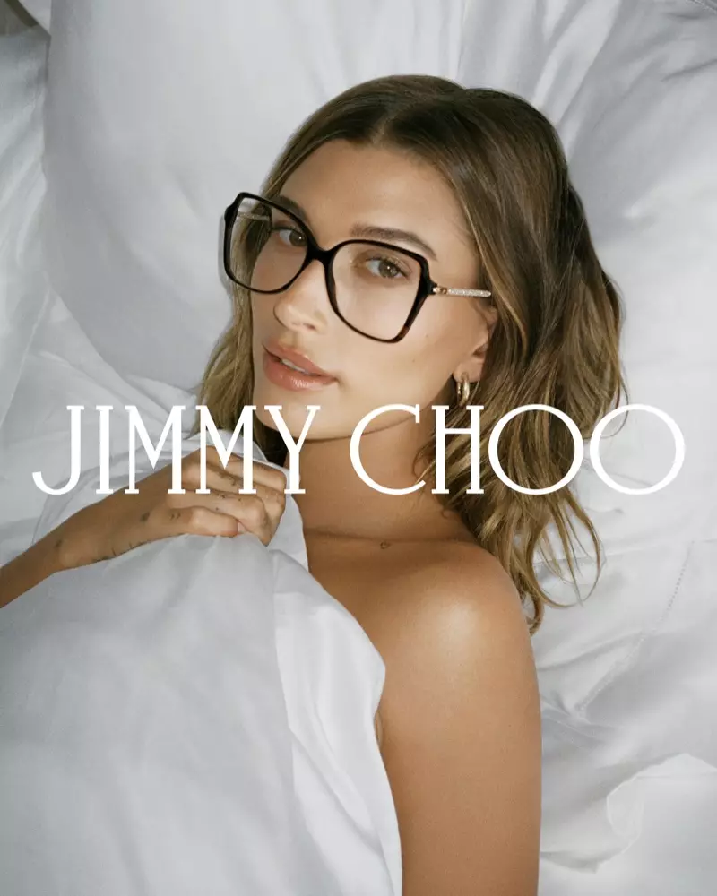 Hailey Bieber poseert in bed en draagt een bril voor de Jimmy Choo herfstcampagne van 2021.