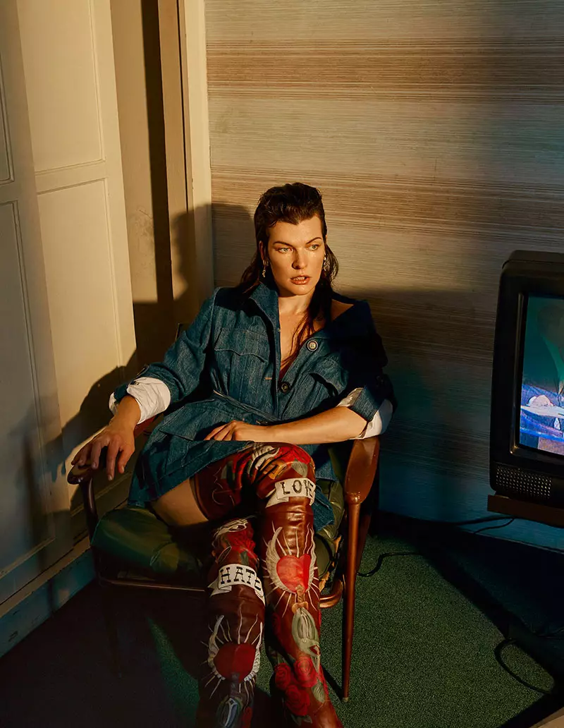 Stând pe un scaun, Milla Jovovich poartă jachetă Miu Miu din denim cu cizme Vetements brodate