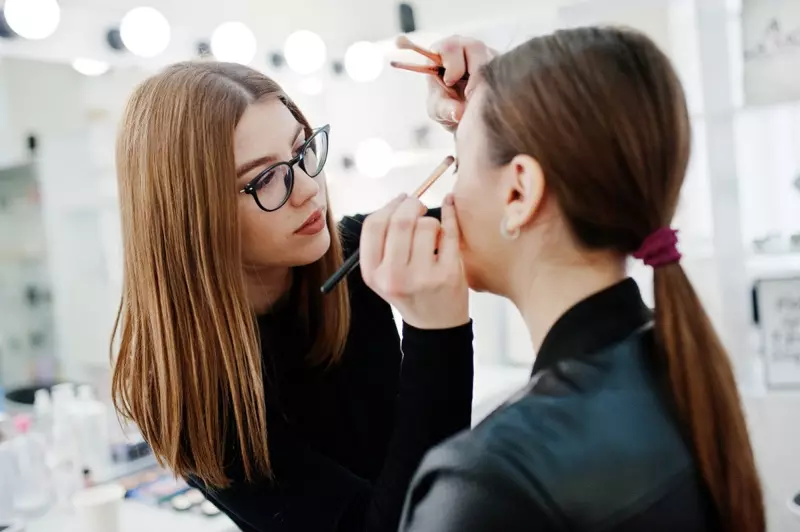 Aantrekkelijke make-upartiest die een bril draagt en make-up op het model aanbrengt