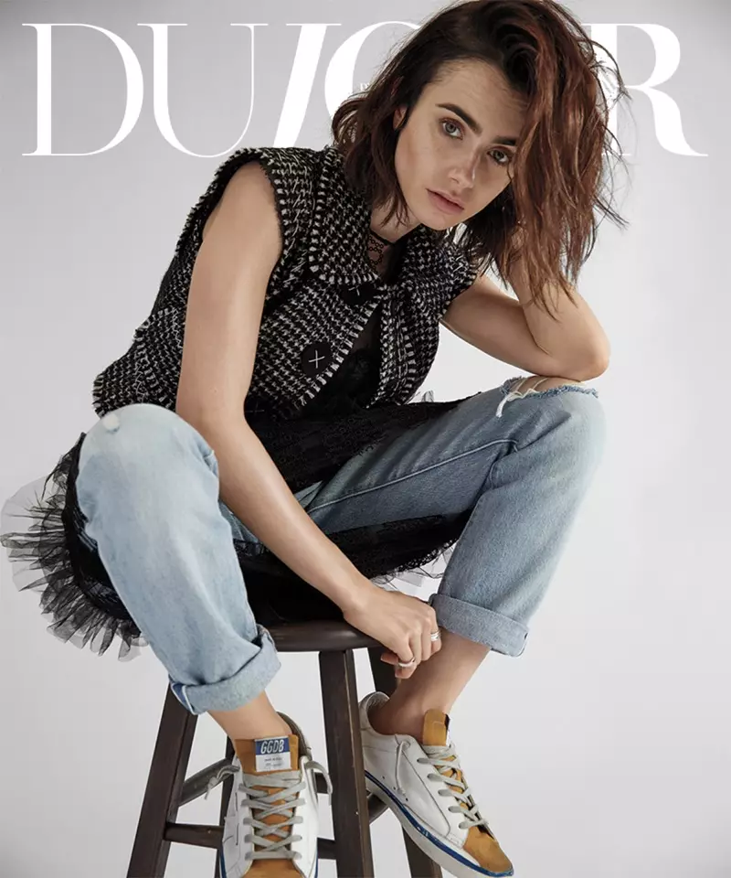 Lily Collins sidder på en skammel og poserer i Dolce & Gabbana-vest, Burberry-kjole, Levi's-jeans og Golden Goose Deluxe Brand-sneakers