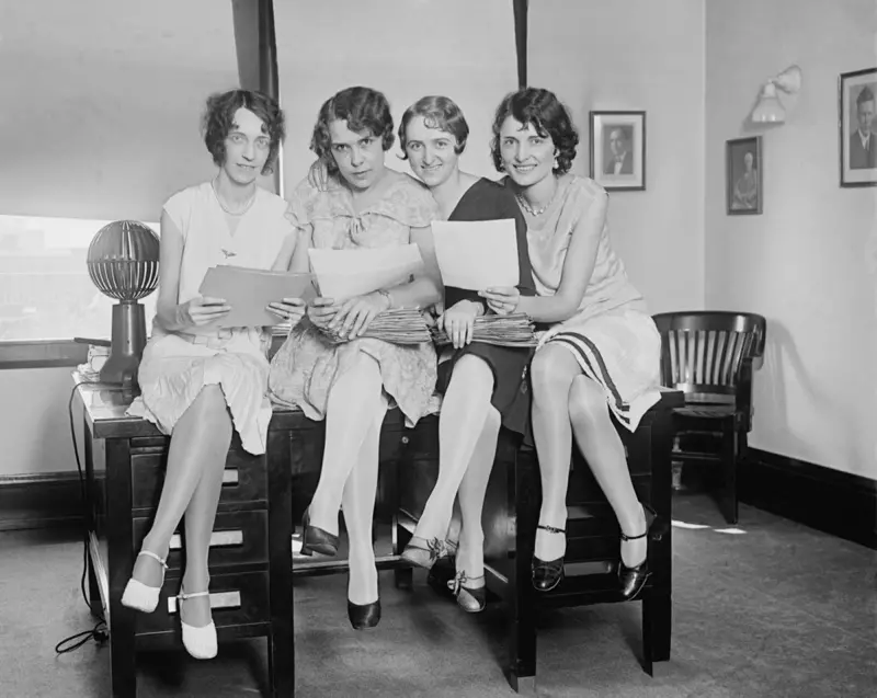 Le giovani donne che lavorano in un ufficio indossano abiti al ginocchio e diversi stili di scarpe nel 1929.
