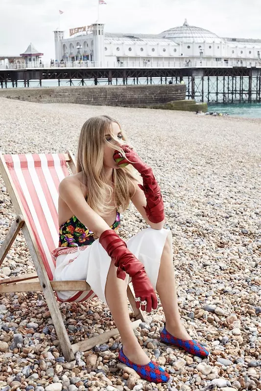 Denisa berpose di pantai dengan sarung tangan merah panjang, kemeja bermotif bunga, dan rok putih