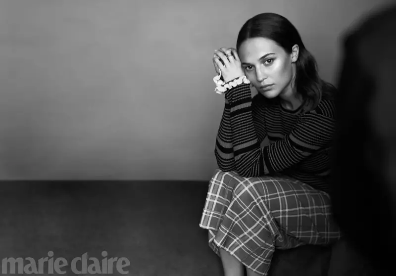 Difoto dalam warna hitam dan putih, blus bergaris Alicia Vikander dan rok kotak-kotak