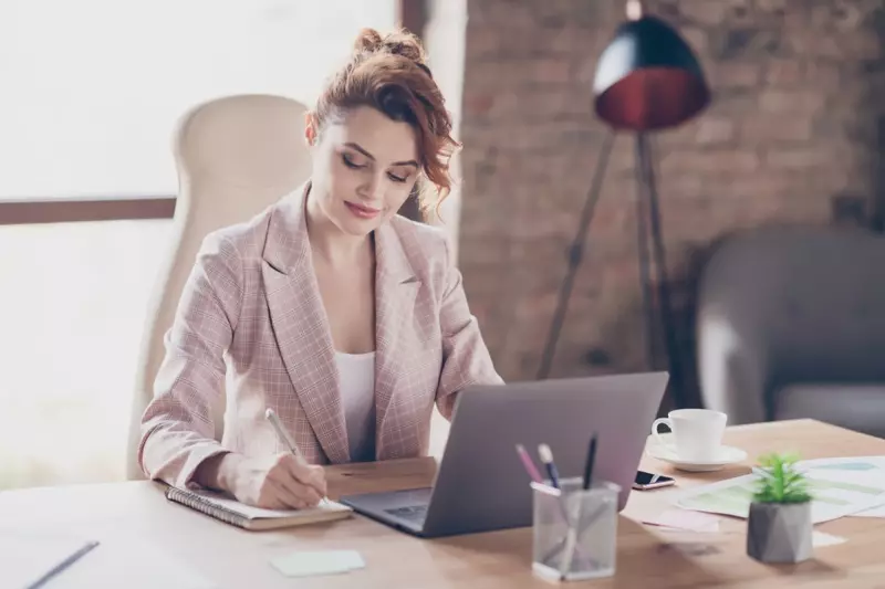 Frauen-Büro-Rosa-Blazer-Laptop-Schreibtisch, der Notizblock schreibt