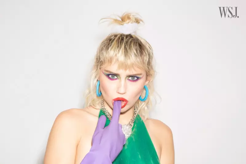 La chanteuse Miley Cyrus montre un haut vert scintillant avec des gants violets.