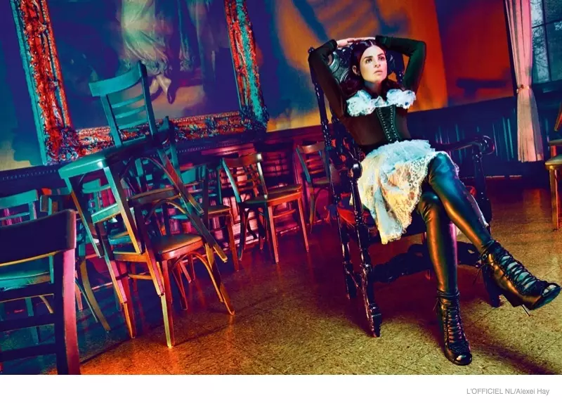 Φορώντας κορσέ και φούστα από Givenchy, η Τζούλια σταυρώνει τα πόδια της σε ένα δωμάτιο γεμάτο καρέκλες.
