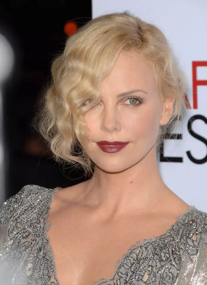 Actrice Charlize Theron huet hir Hoer an tousled Fanger Wellen an engem modernen, 1920er inspiréiert Updo.