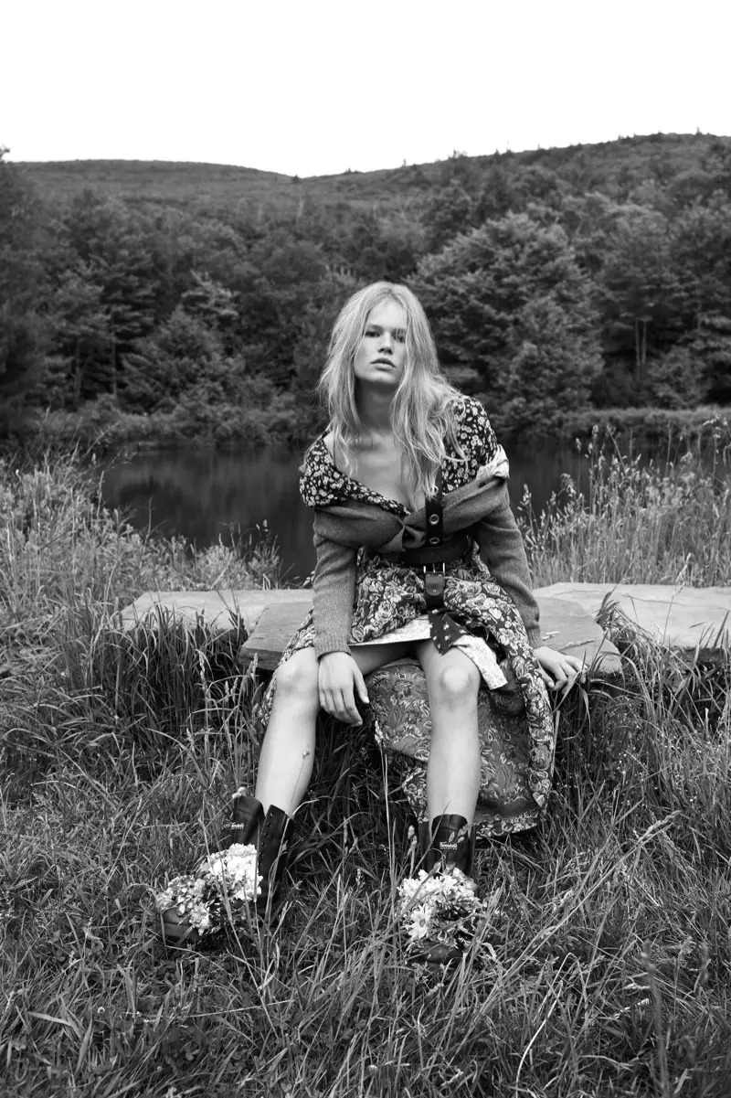 Anna Ewers, dy't bûtendoar posearret, modelleart in cardigan en florale rok fan Miu Miu