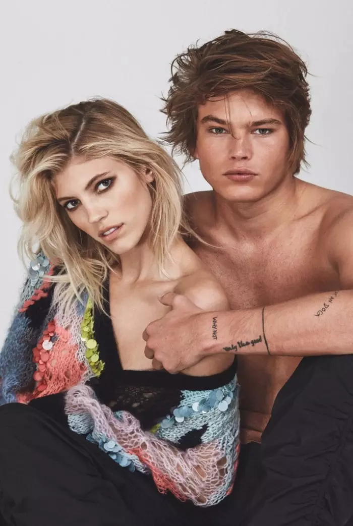 Devon Windsor yn ystumio wrth ymyl Jordan Barrett mewn siwmper Versace