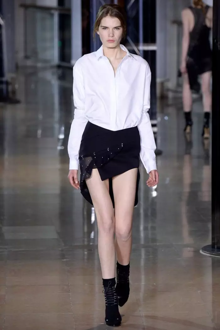 Uma modelo desfila na passarela do desfile outono-inverno 2016 de Anthony Vaccarello vestindo uma camisa branca com uma saia preta assimétrica