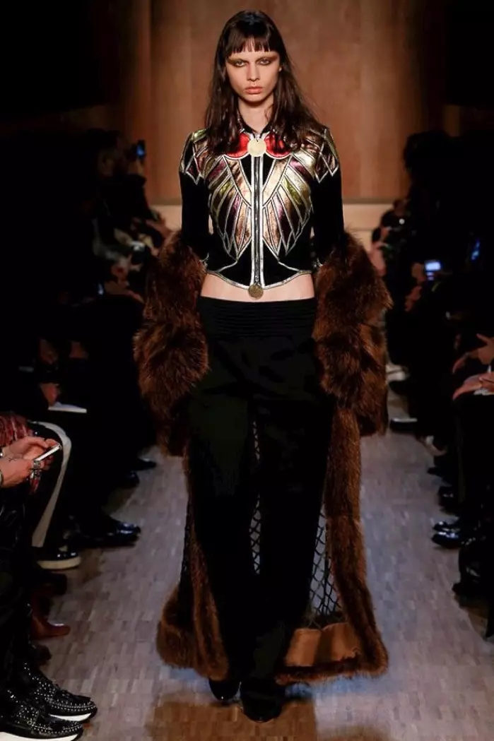 Modelka chodzi po wybiegu na pokazie Givenchy jesień-zima 2016 w metalicznej kurtce ze skrzydłami, futrzanym płaszczu i czarnych spodniach