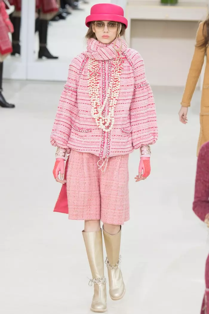 Una modelo camina por la pasarela del desfile otoño-invierno 2016 de Chanel con una chaqueta y falda de tweed rosa y botas doradas.