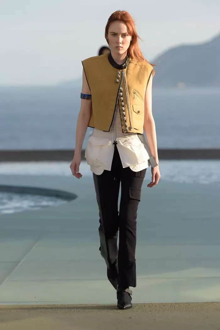 2017 루이 비통 리조트 쇼에서 모델이 크롭 베스트, 롱 블라우스, 꼭 맞는 바지를 입고 런웨이를 걷고 있습니다.