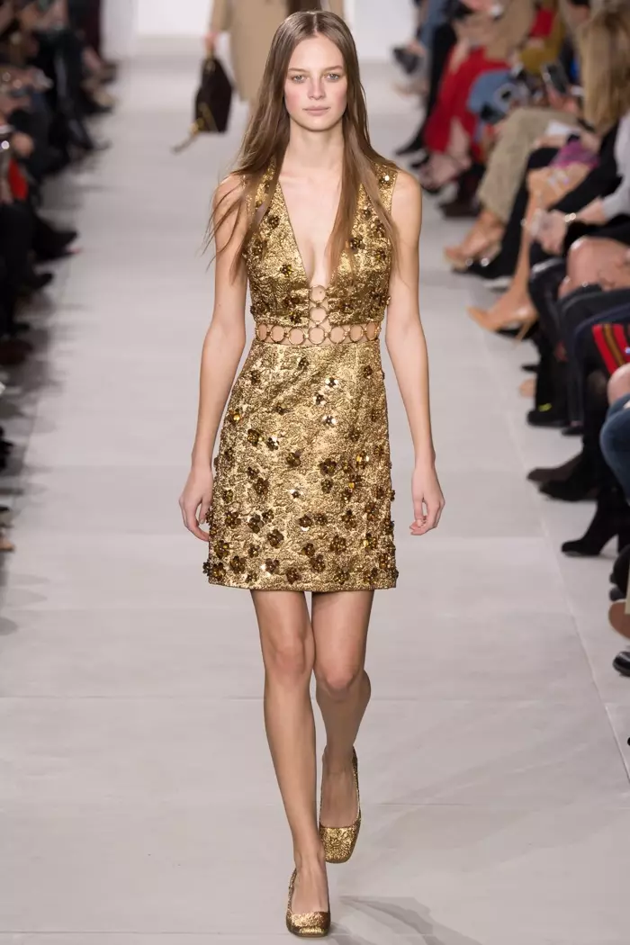 Modelka spaceruje po wybiegu w złotej sukience na zmianę z kolekcji Michaela Korsa jesień-zima 2016