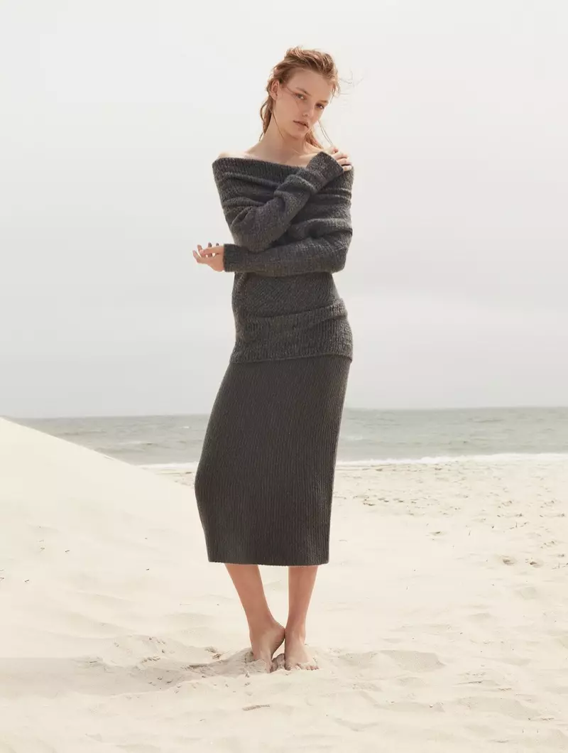 Berpose di pantai, Roos Abels mengenakan sweater dan rok kasmir off-the-shoulder Calvin Klein Collection