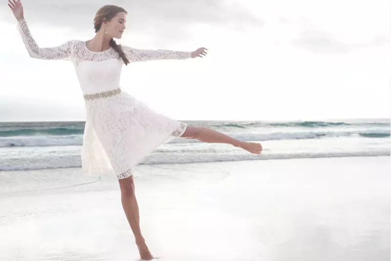 Unha modelo posa na praia cun vestido branco de encaixe