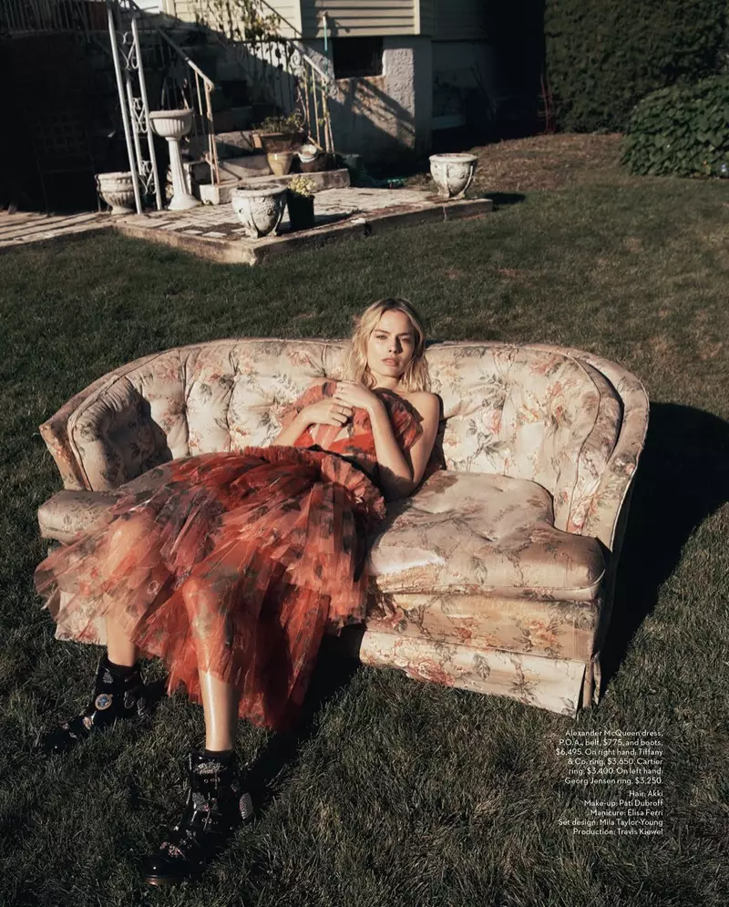 Akiweka kwenye sofa, Margot Robbie amevaa mavazi ya Alexander McQueen, ukanda na buti